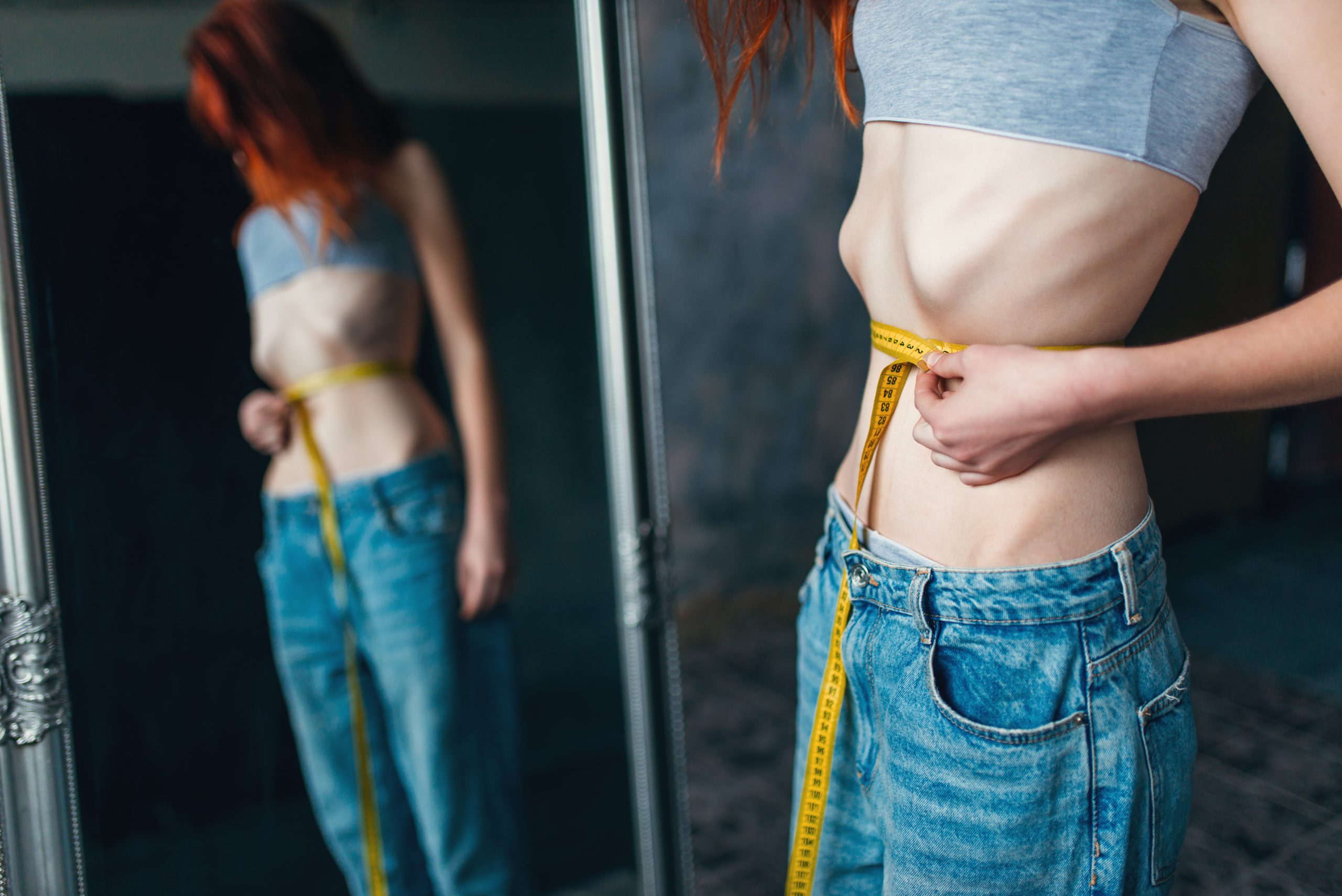 Woman measures waist against mirror, weight loss