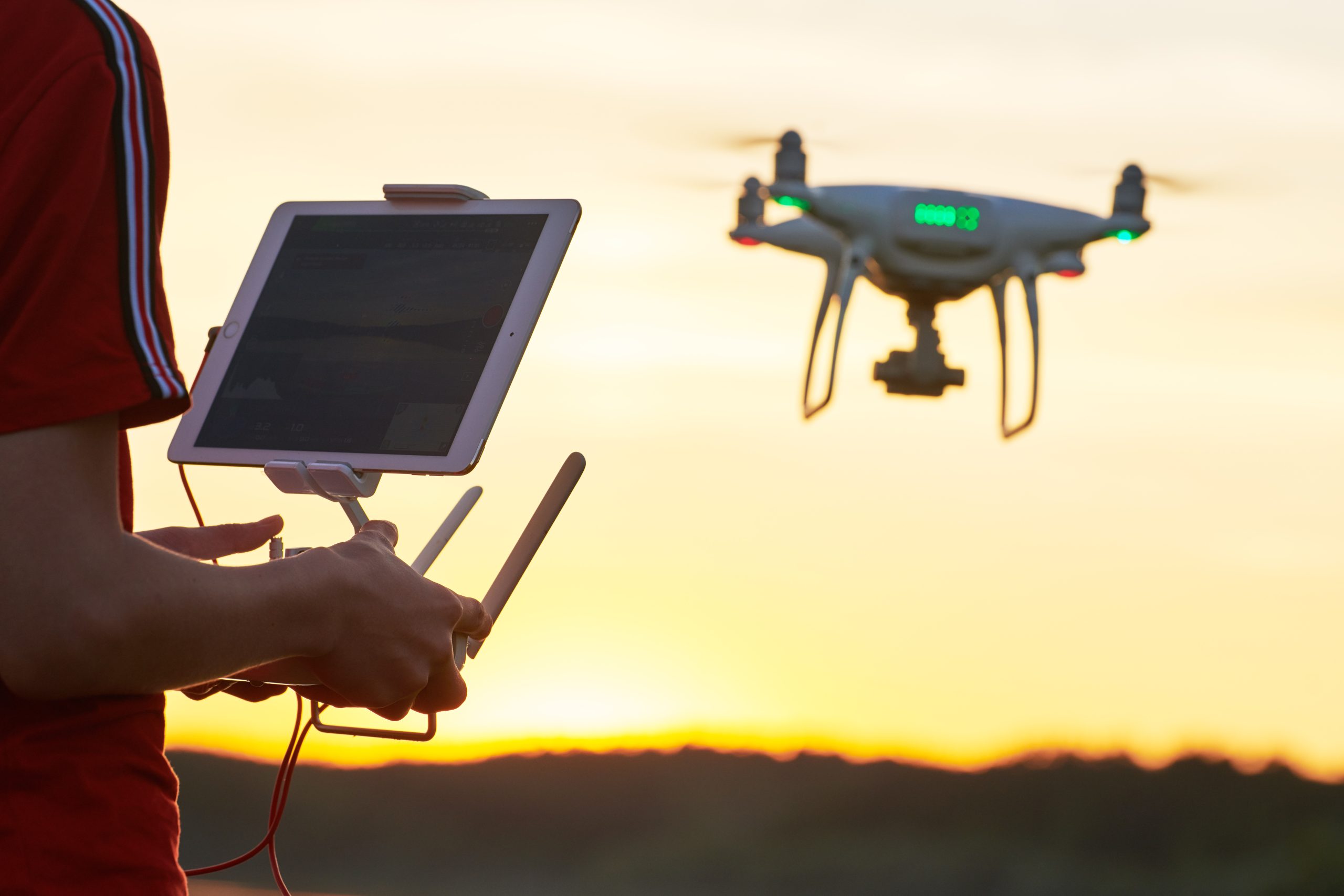 operator piloting flying copter drone at sunset. Focus on remote controller